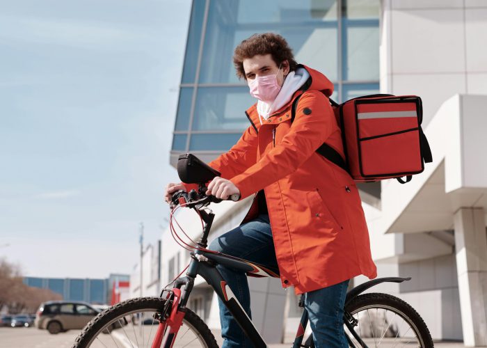 pexels-photo-4392030-4392030 Male delivery cyclist in city wearing face mask and orange coat